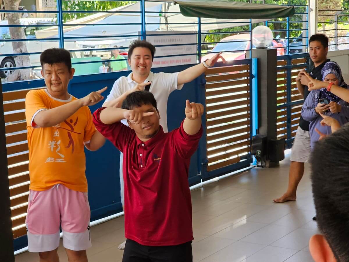 Two residents and a MedicalMet colleague copying a dance move together at the PKKII Insan special needs home in Kuala Lumpur