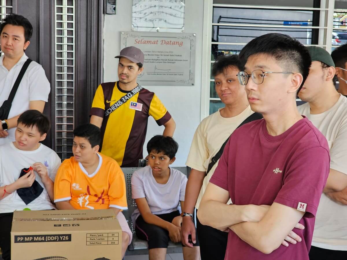 Residents and MedicalMet volunteers standing beside the Selamat Datang plaque inside the PKKII Insan home in Kuala Lumpur during the MedicalMet CSR visit
